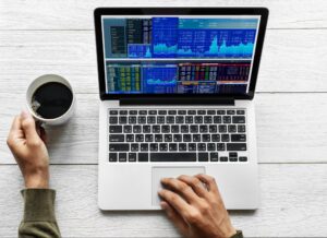 Person using laptop with a CFD trading terminal open while their left hand holds a cup of coffee.