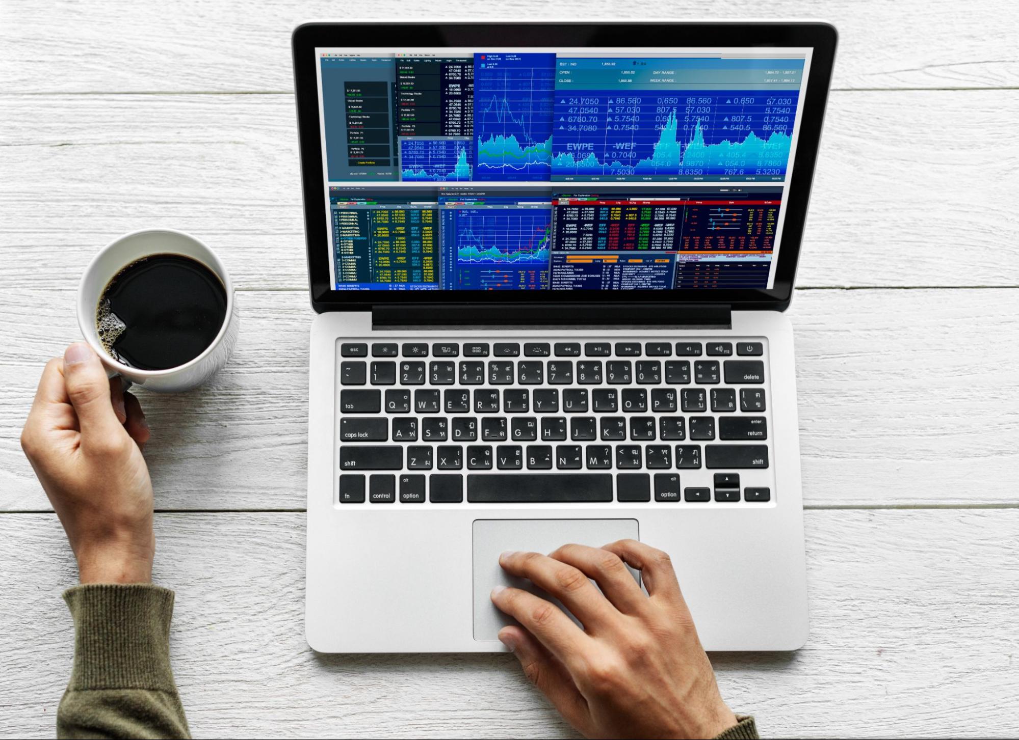 Person using laptop with a CFD trading terminal open while their left hand holds a cup of coffee.