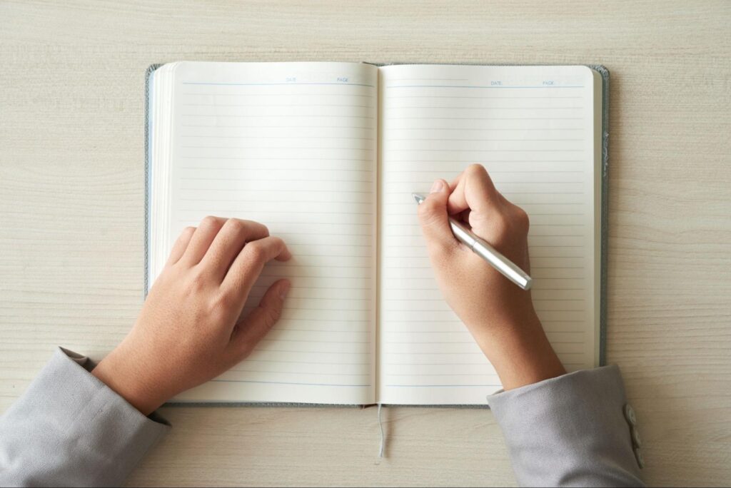 Image of a person holding a pen ready to write in a blank notebook.